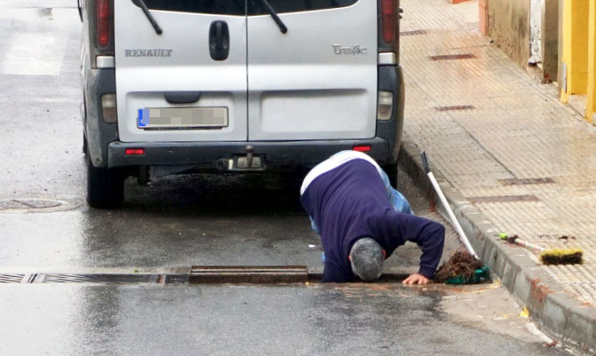 Un vecino limpia una rejilla de recogida de pluviales en la bda. Virgen del Oro